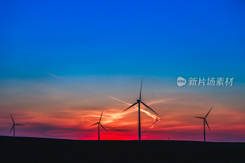 夕阳下蓝红的天空下，农田上的风力涡轮机农场