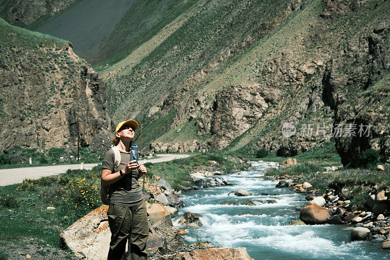 女背包客在峡谷里的山河边喝水