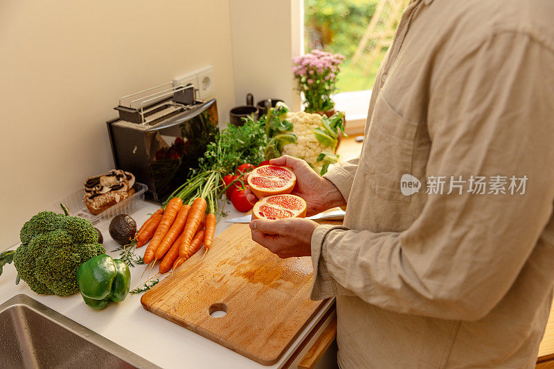 在厨房里，年轻人的手拿着半个红葡萄柚——准备生素食食谱——特写镜头