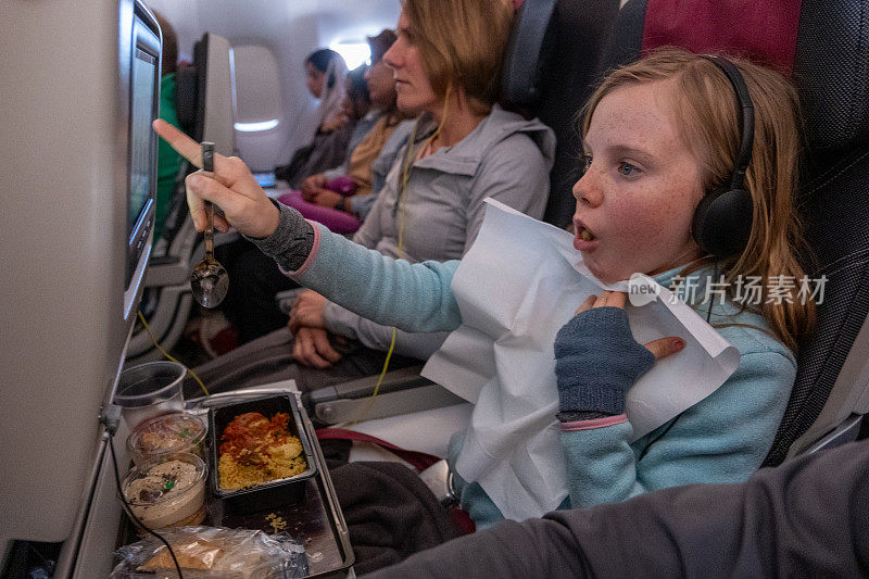 女孩一边吃饭一边欣赏飞机上的电影
