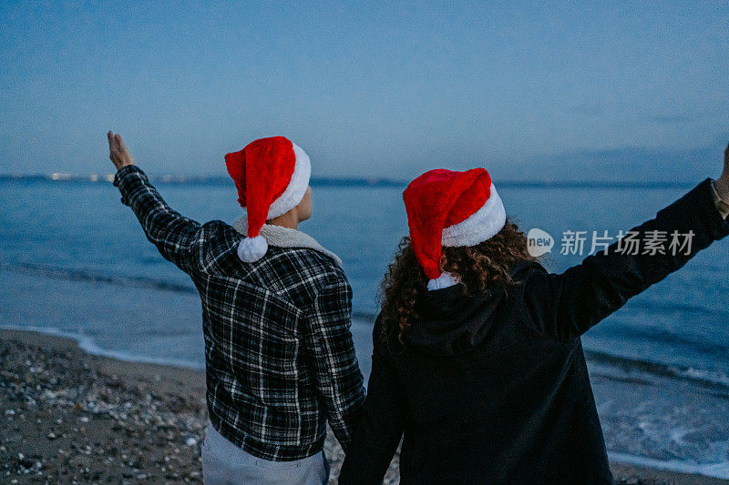 希腊，一对戴着圣诞帽的年轻夫妇在黎明时分欣赏着海岸线的景色