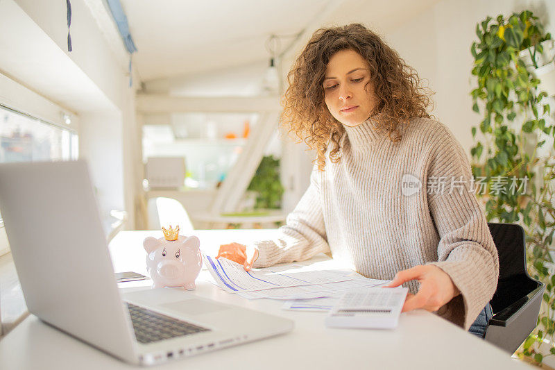 年轻女子使用计算器，同时通过账单和家庭财务