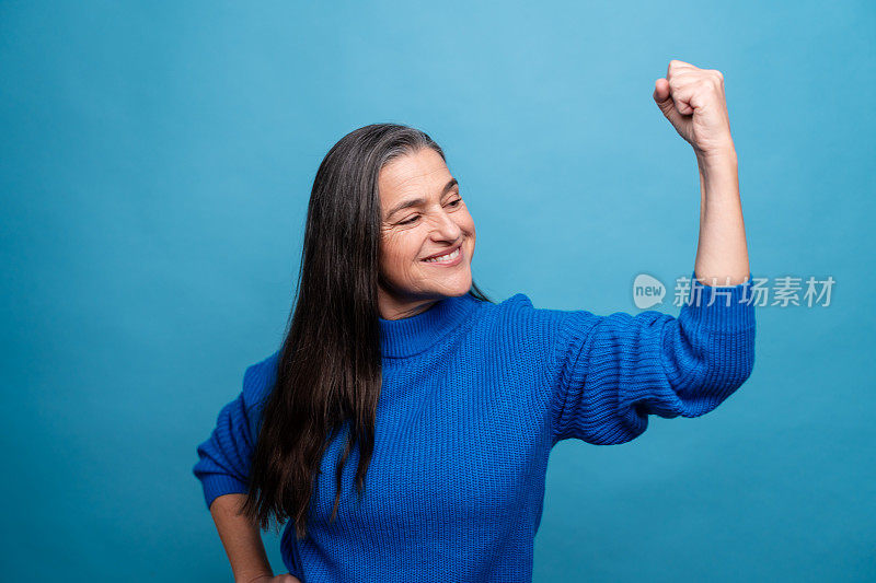 快乐的成熟女性在蓝色背景下高举双臂庆祝成功。