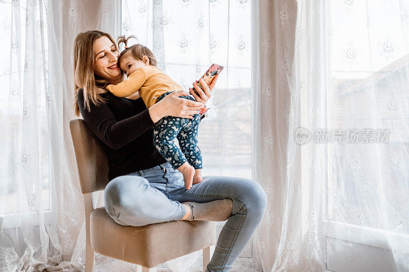 这位母亲把孩子抱在腿上，看着她的智能手机。