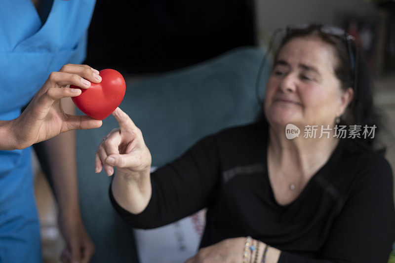 年长的妇女拿着心形图案，年轻的男护士扶着她