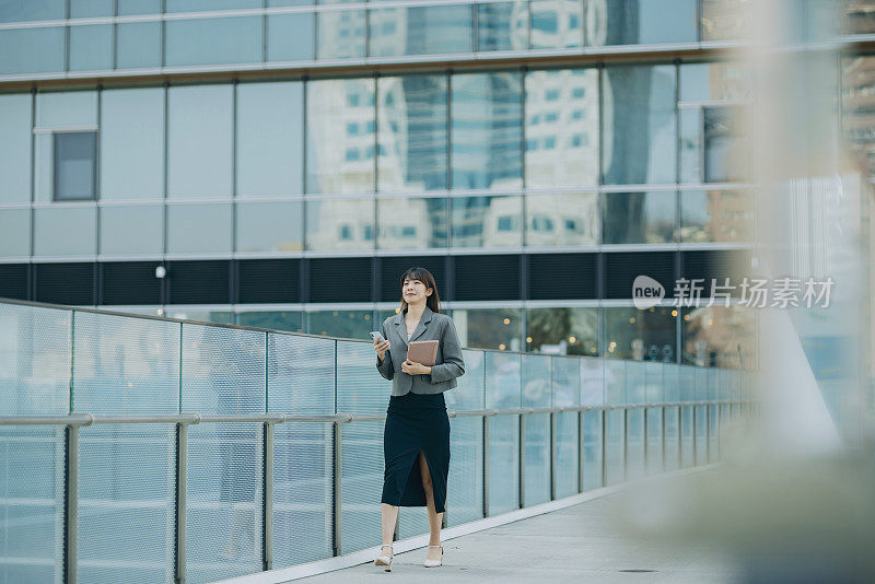 自信的年轻亚洲女商人带着智能手机四处奔波