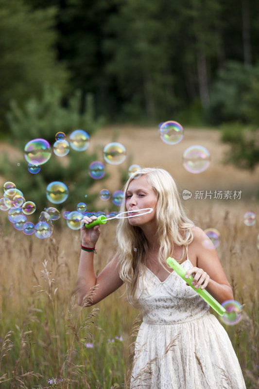 美丽的少女吹乡村自然田野的泡沫