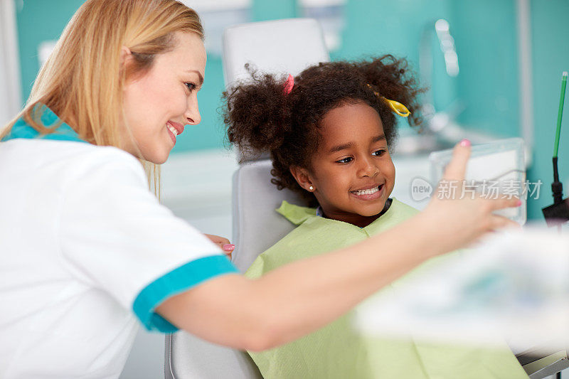 坐在牙科椅上的女孩对着镜子里的牙医展示牙齿