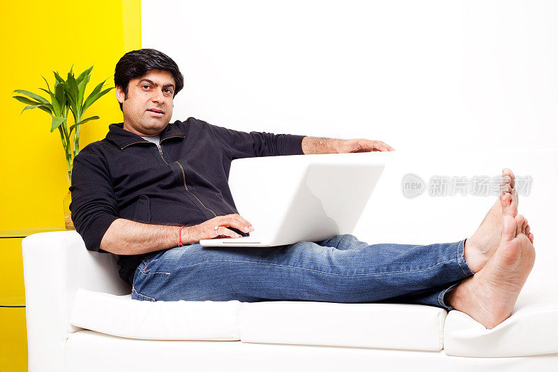休闲的亚洲印度人坐在沙发上使用笔记本电脑