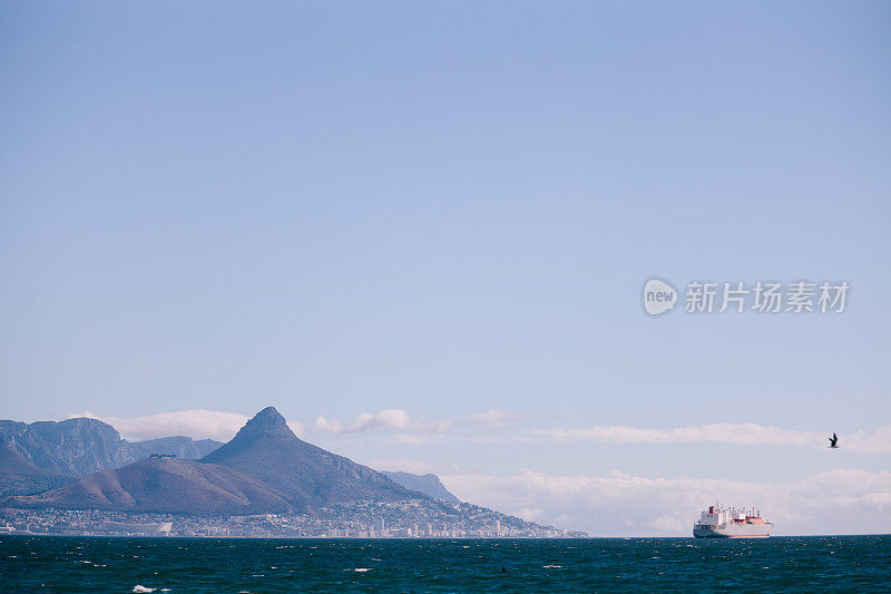 日落时分，多山的海岸外有一艘集装箱船