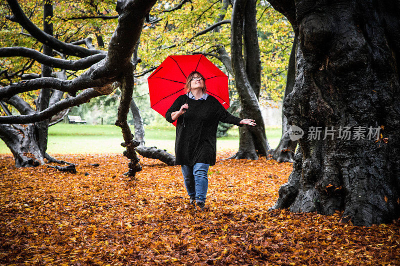 女人撑着红伞走过秋叶
