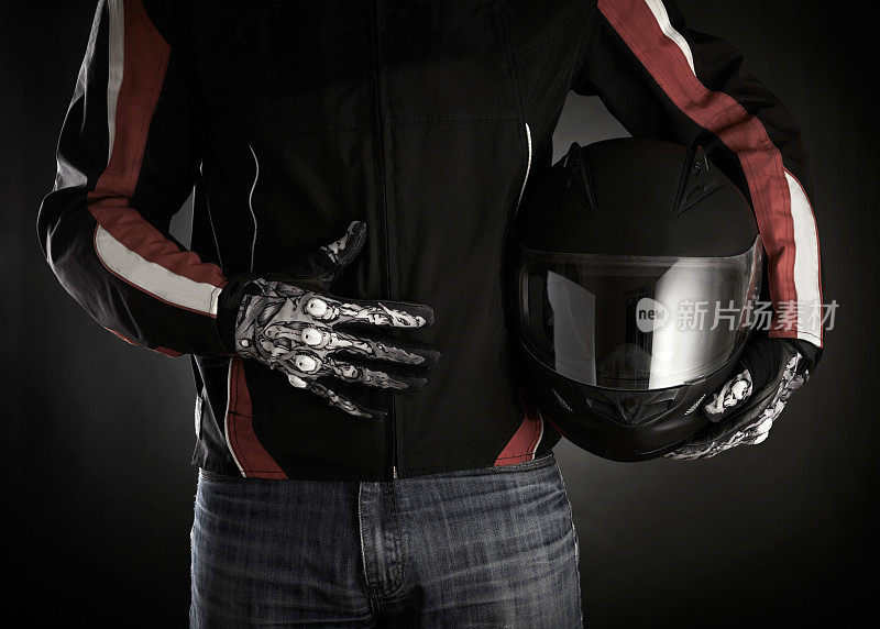 摩托车手，手里拿着头盔。暗的背景