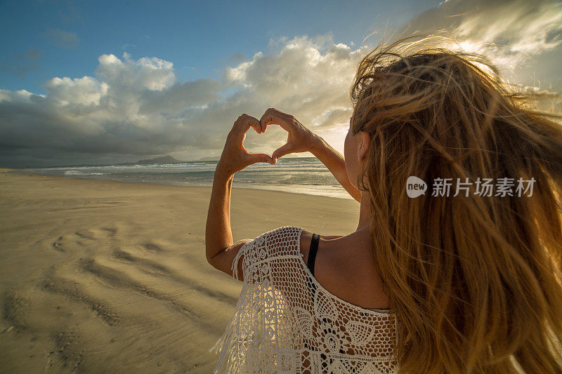 海滩上的女性向夕阳做出心形的指架