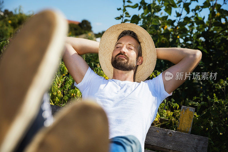 一个人靠着院子里的植物坐在木凳上休息