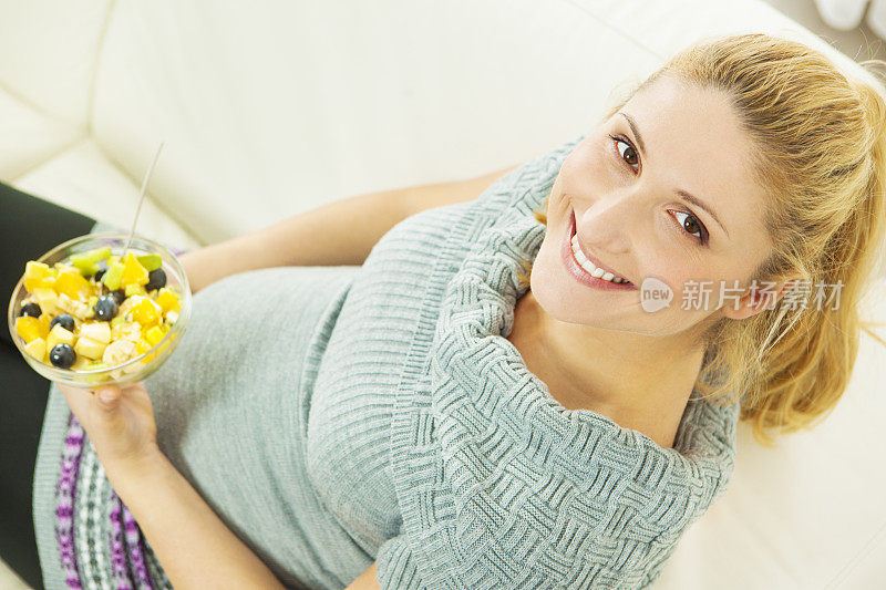 快乐的年轻孕妇吃水果沙拉