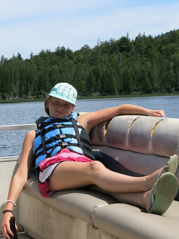 十几岁的女孩穿着救生衣拿着瓶子在平底船上休息