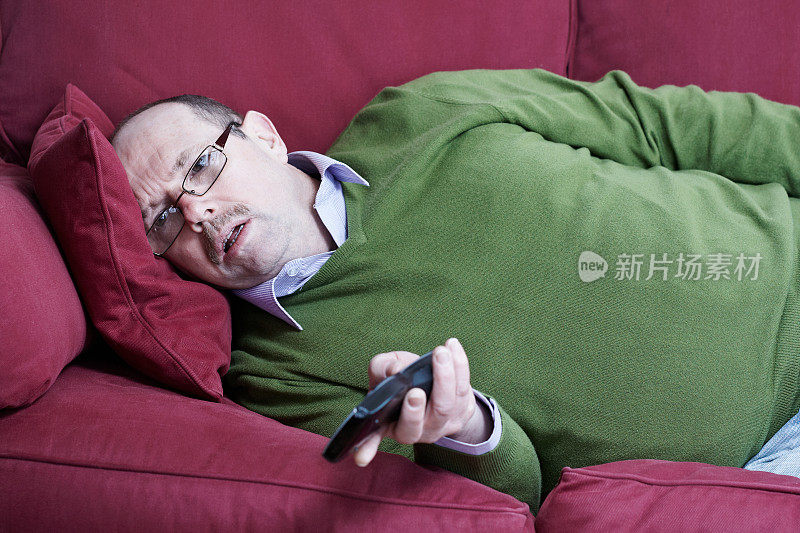 成熟男子肖像躺在沙发上与电视遥控器