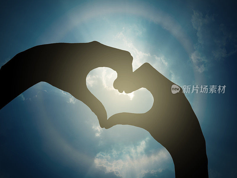 两只手在日冕上做一个心形，蓝色的天空映衬着云朵，这就是情人节爱情的概念
