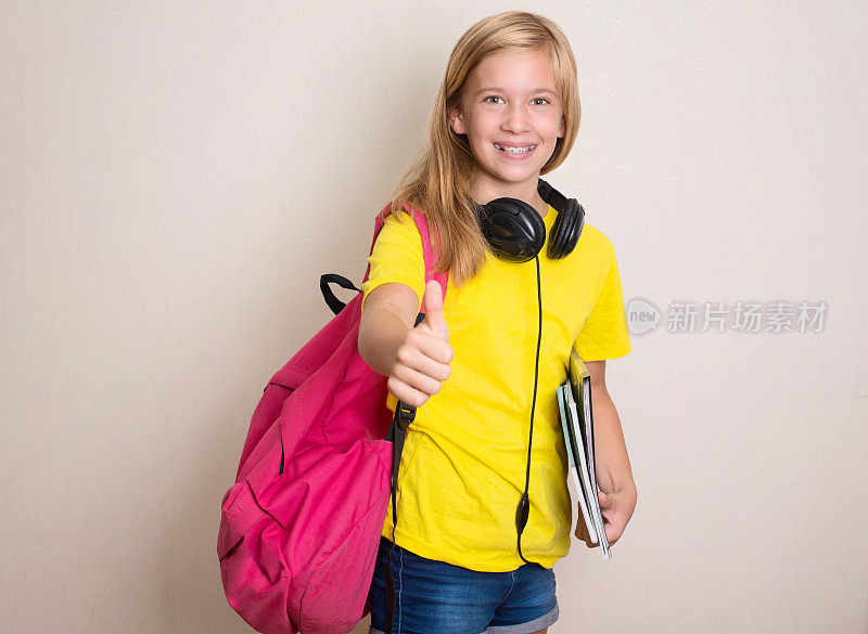 十几岁的女孩学生在黄色t恤与背包和耳机微笑。教育。