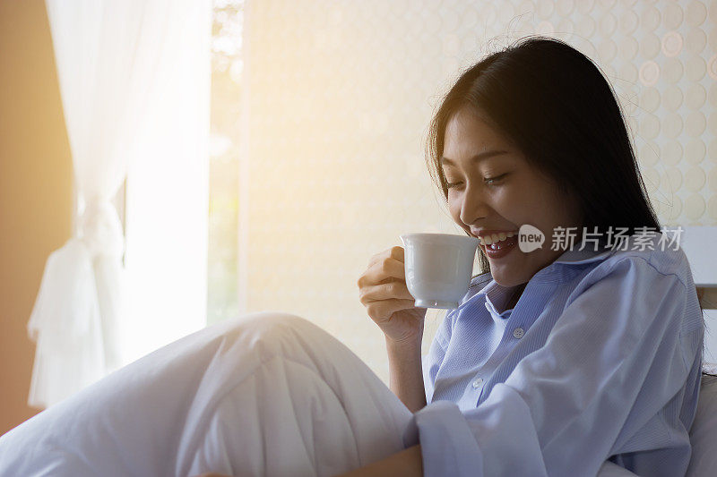 快乐的亚洲女人在床上喝咖啡
