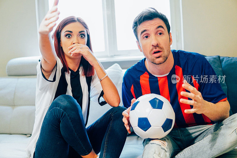 一对惊讶的夫妇在电视上看足球比赛