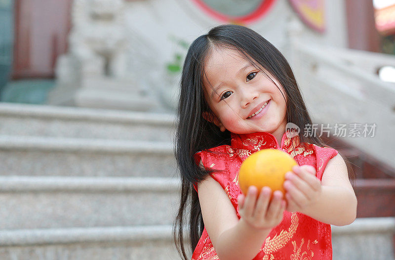 在泰国曼谷的中国寺庙，微笑的亚洲小女孩穿着传统的中国服装，拿着神圣的橘子，中国新年的概念。