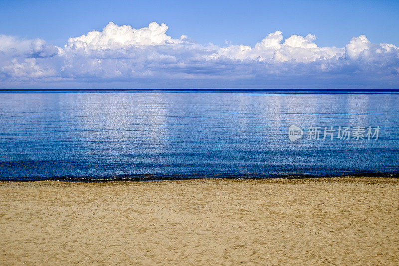 希腊克里特岛的沙滩上，云朵倒映在平静的海面上