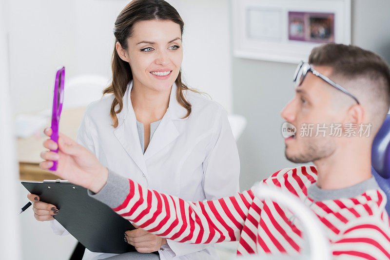 微笑的女牙医听评估的病人，而他看着镜子和检查他的牙齿在医院