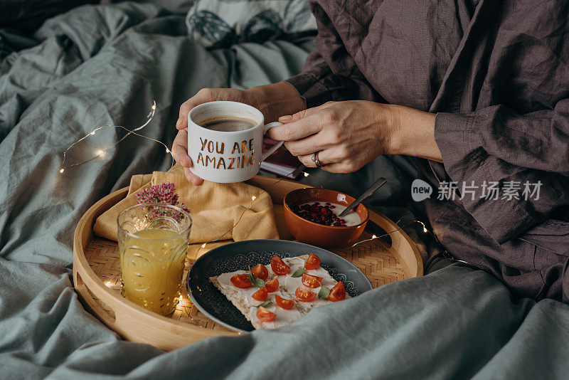 女人在床上用托盘吃早餐，端着咖啡和食物