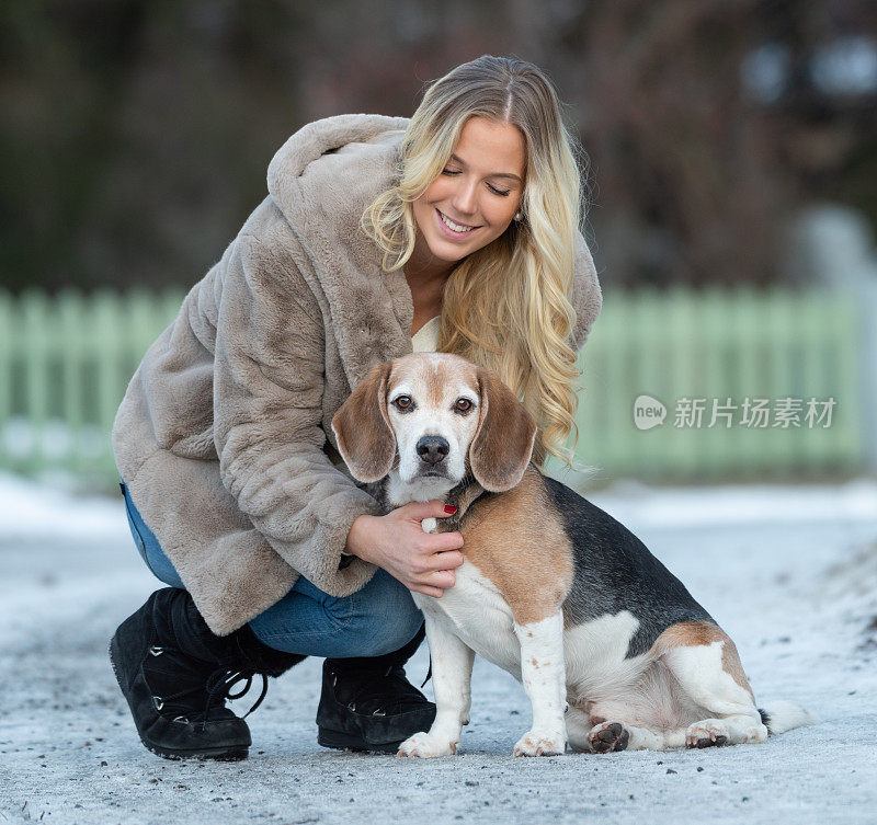 一个金发年轻女人和她的小猎犬在冬天的街道上