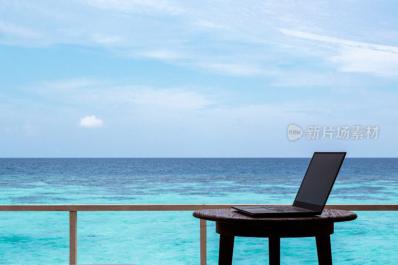 桌上一台电脑的剪影。清澈的蓝色热带海水作为背景