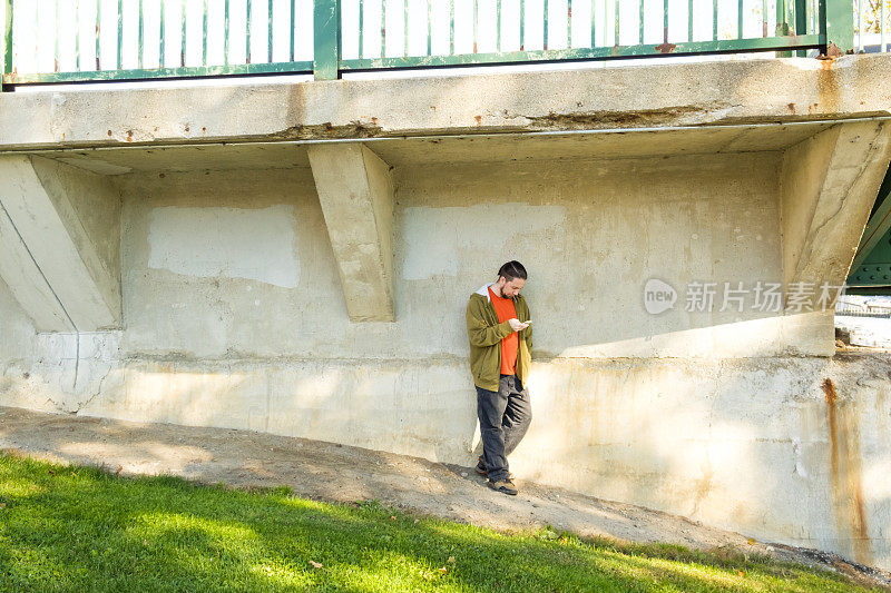 一名男子站在旧水泥桥旁看智能手机