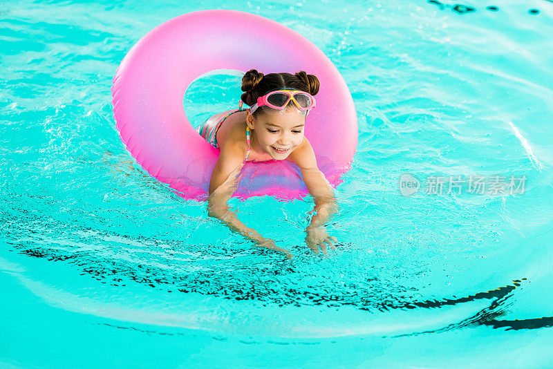 快乐的孩子在游泳池里用充气圈学习游泳