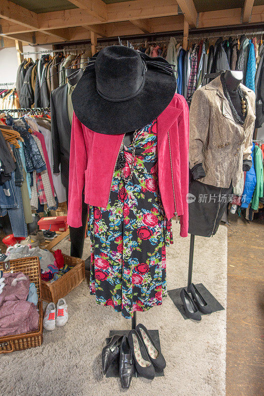 在旧货店出售的带有粉红色夹克和黑色帽子的花裙子