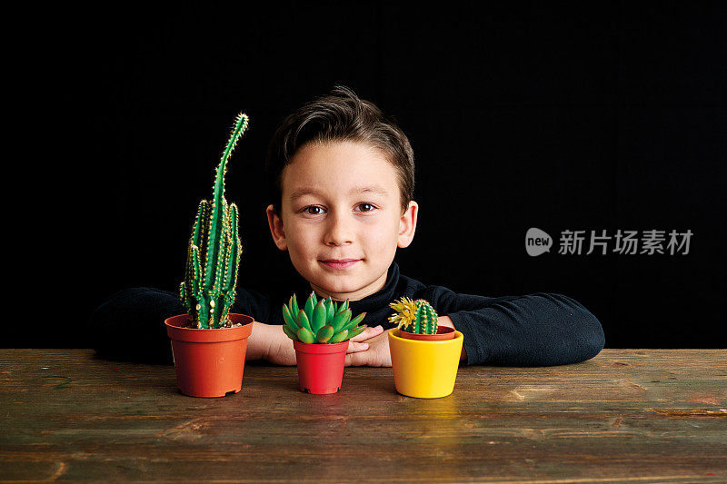 6-7岁的可爱的孩子坐在桌子上，看着他的植物在黑色的背景。