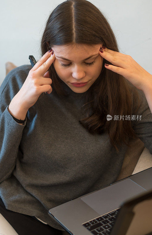 一个头痛的女人抱着她的头在笔记本电脑上