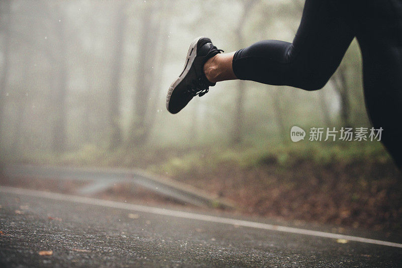 一个不知名的运动员在雨天在马路上慢跑。
