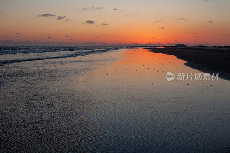 在日落后的海滩上，橙色的辉光在沙滩上反射出浅浅的海浪