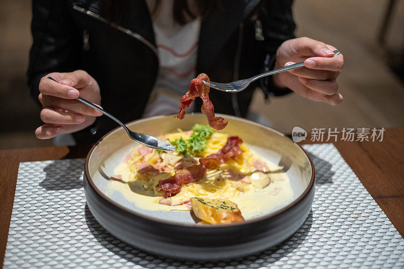 年轻的亚洲女人正在吃意大利通心粉和脆培根