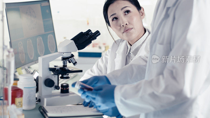 未来实验室内部。亚洲女医生在基因研究期间与伴侣