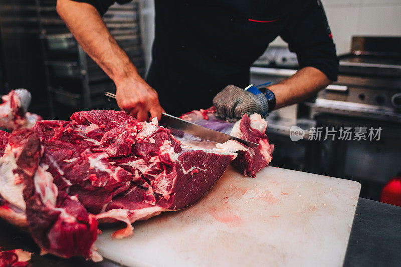 男屠夫在餐厅厨房用刀切生牛肉