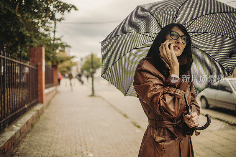 一位漂亮的商务老妇人在雨中行走，手里拿着手机