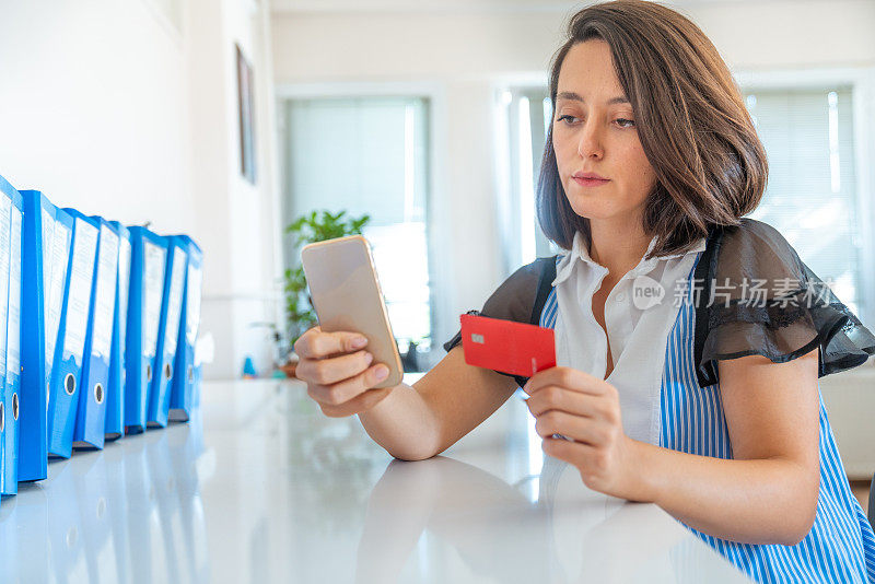 年轻的女商人正在用信用卡用手机购物