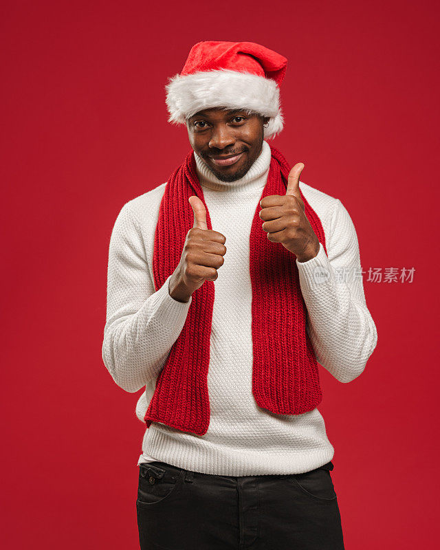 一个穿着羊毛衫、戴着圣诞帽、皮肤黝黑的年轻男子微笑着竖起大拇指