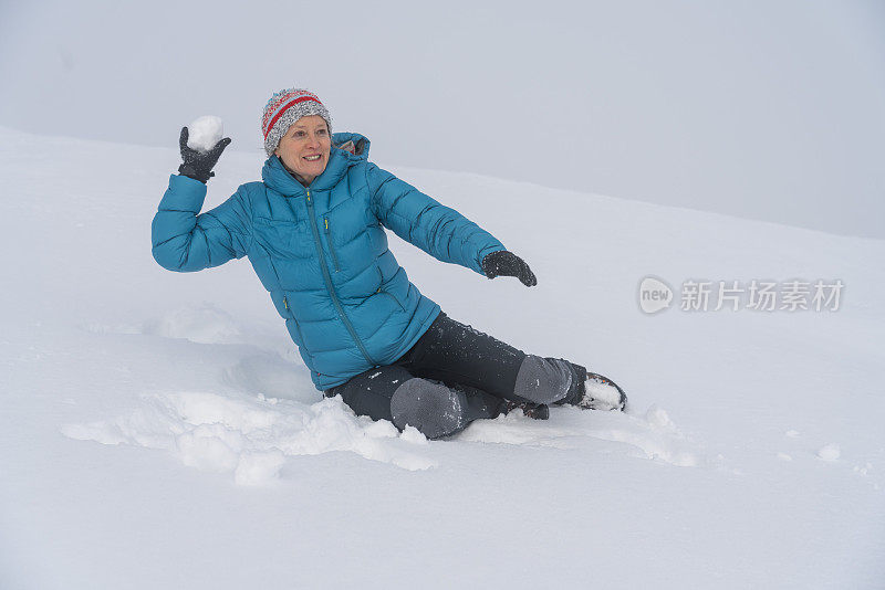 成熟的女人穿着皮大衣在雪地里扔雪球