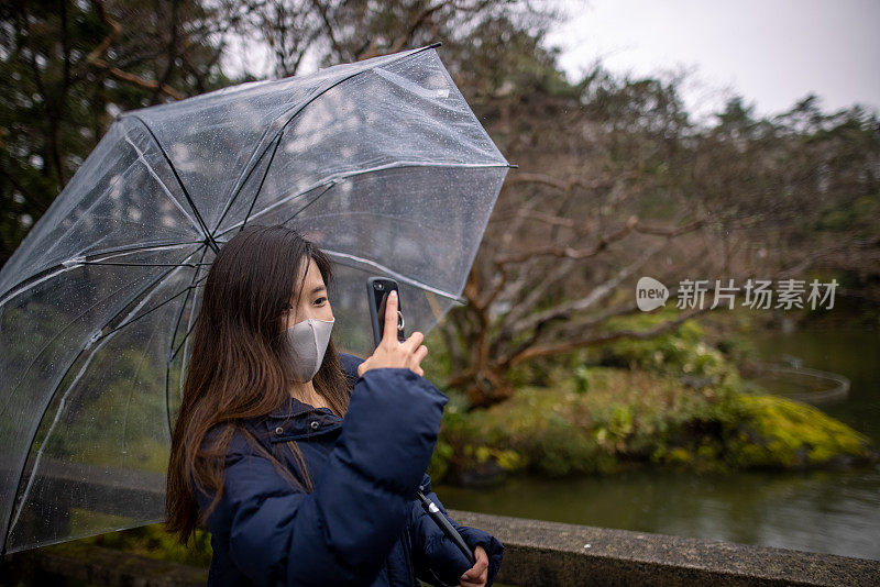 年轻女子戴着保护面罩在池塘周围拍照