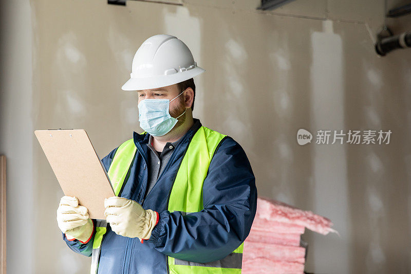 建筑工人或工程师在工地上搬运材料并查看剪贴板上的平面图