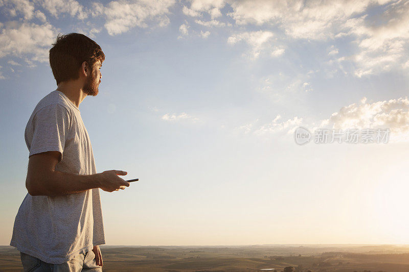 夕阳西下时，一个年轻人站在山顶眺望地平线。想象未来。