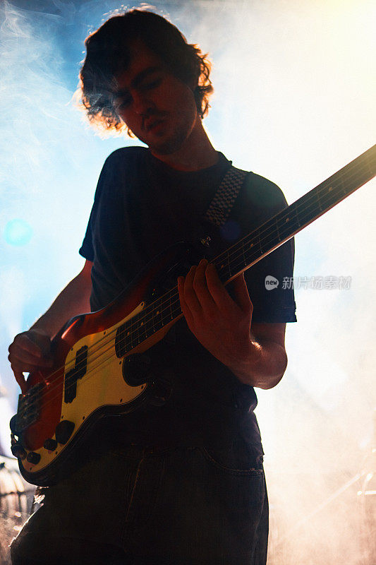 一个年轻人在一场摇滚表演的舞台上热情地弹着贝斯吉他