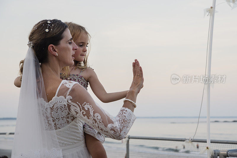 新娘在海边和穿着花裙子的小女儿跳舞。